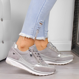 Scarpe da ginnastica grigie da donna con dettagli metallici, indossate con jeans chiari strappati. Design moderno e casual per look alla moda.