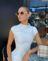 Woman wearing gold-rimmed sunglasses with white top and purse